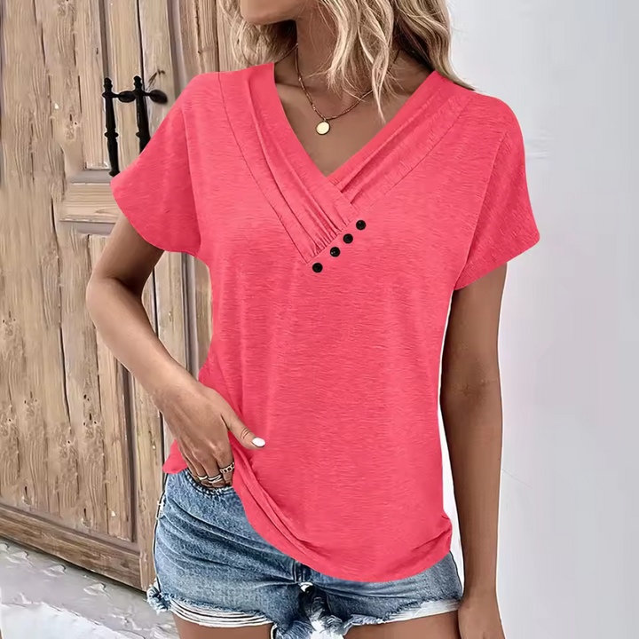 Frau in rotem V-Ausschnitt-T-Shirt mit Knöpfen, kombiniert mit blauen Jeansshorts, steht vor Holztür. Sommermode, lässiger Stil.