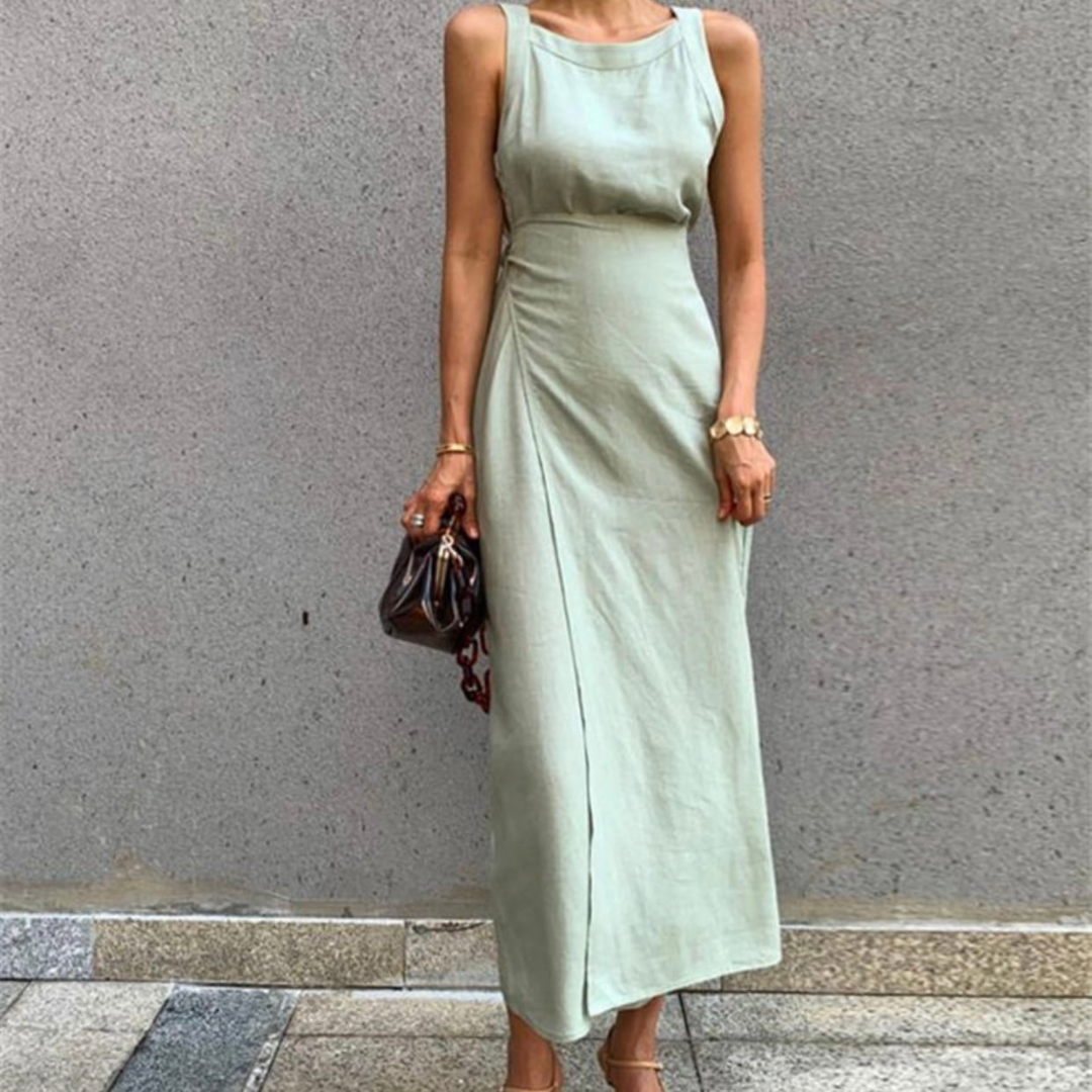 Frau in elegantem, ärmellosem, hellgrünem Maxikleid mit brauner Handtasche vor grauer Wand. Sommermode, Damenkleidung, stilvoller Look.