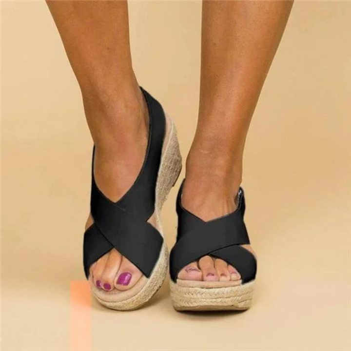 Schwarze Damen-Wedges mit Bastsohle, offene Zehen, gekreuzte Riemen, modische Sommerschuhe, Nahaufnahme, beige Hintergrund.