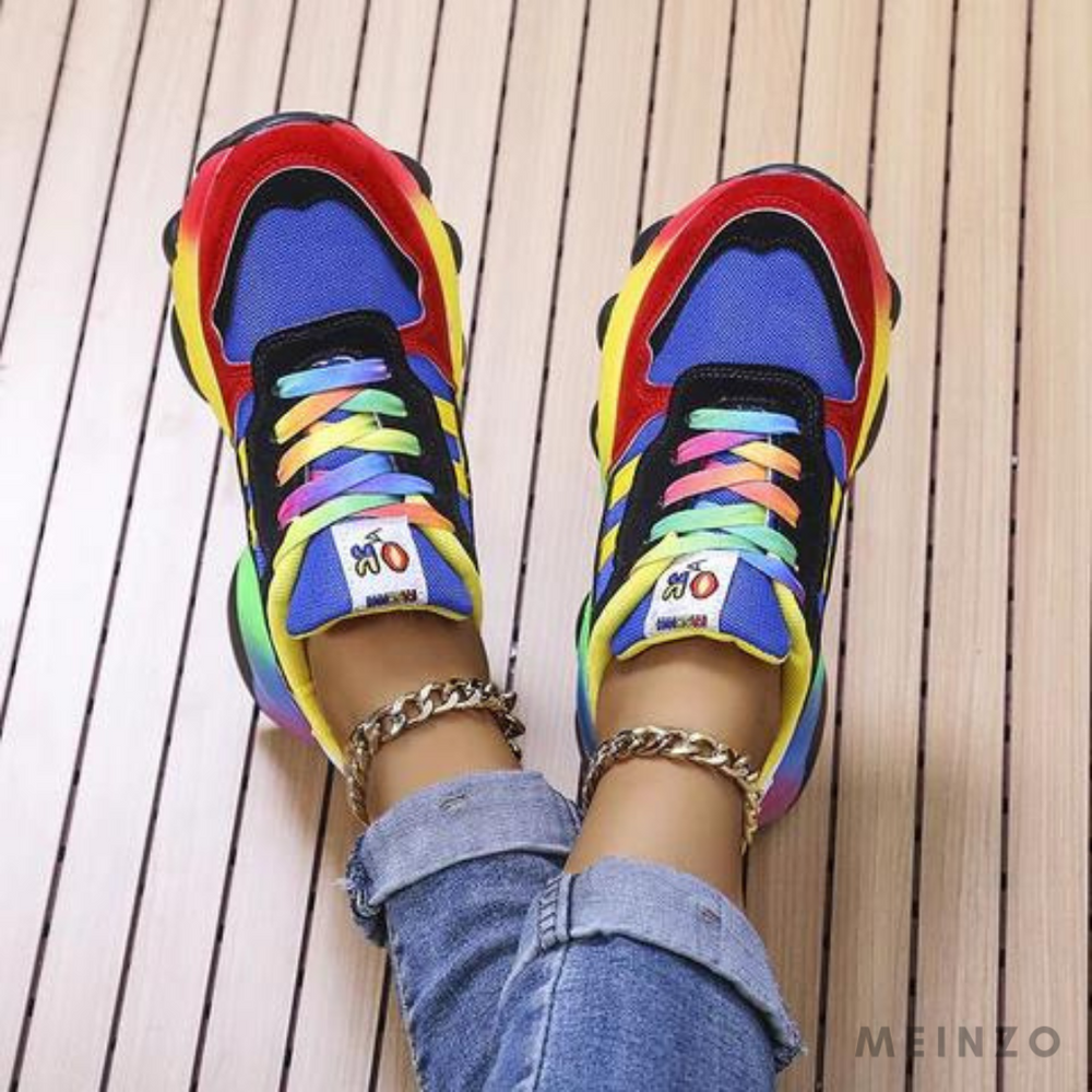 Bunte Sneaker mit Regenbogen-Schnürsenkeln auf Holzfußboden, getragen von Person in Jeans. Modische, farbenfrohe Turnschuhe, trendiges Schuhwerk.