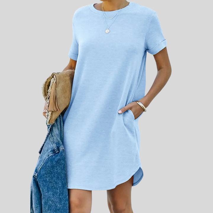 Frau in hellblauem T-Shirt-Kleid mit Taschen, hält eine Jeansjacke und eine braune Tasche. Modetrend, lässiger Sommerlook, Damenbekleidung.