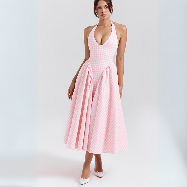 Frau in rosa kariertem Sommerkleid mit tiefem Ausschnitt, knielang, elegant, modisch, vor weißem Hintergrund, trägt weiße Schuhe.