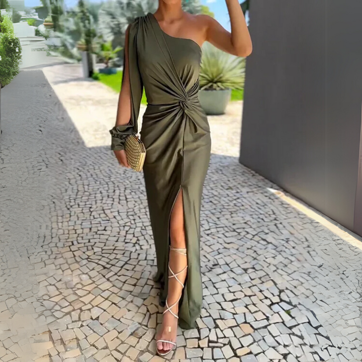 Frau in elegantem, olivgrünem, schulterfreiem Abendkleid mit Knoten-Detail und hohem Schlitz, hält goldene Clutch, trägt Sandalen mit Riemchen.