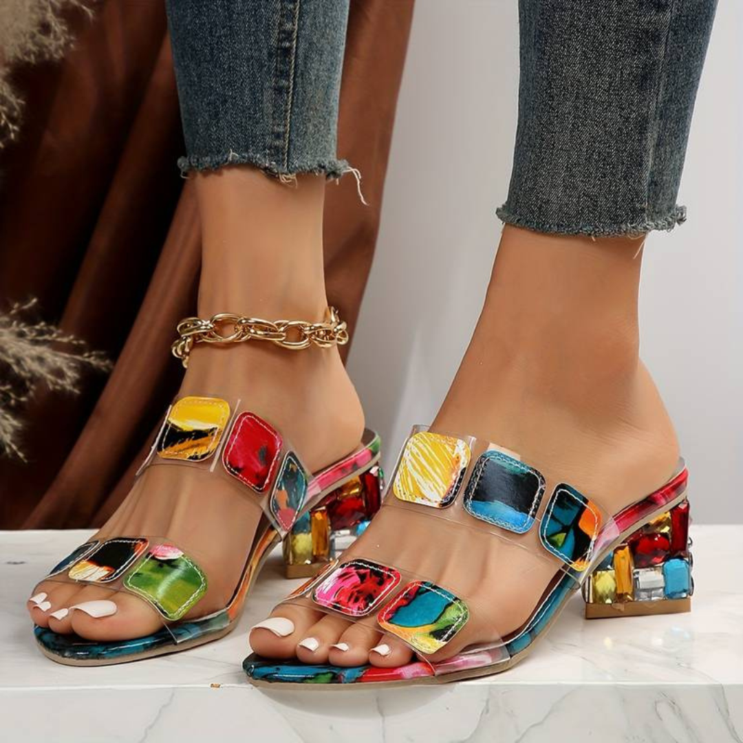 Bunte Sandaletten mit Blockabsatz und quadratischen Mustern, getragen von einer Person in Jeans. Modische Damenschuhe, ideal für Sommertrends.