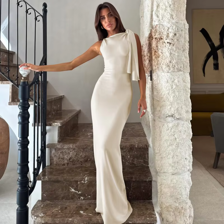 Frau in elegantem, cremefarbenem Abendkleid posiert auf Marmortreppe; modernes Interieur, stilvolle Mode, luxuriöses Design.