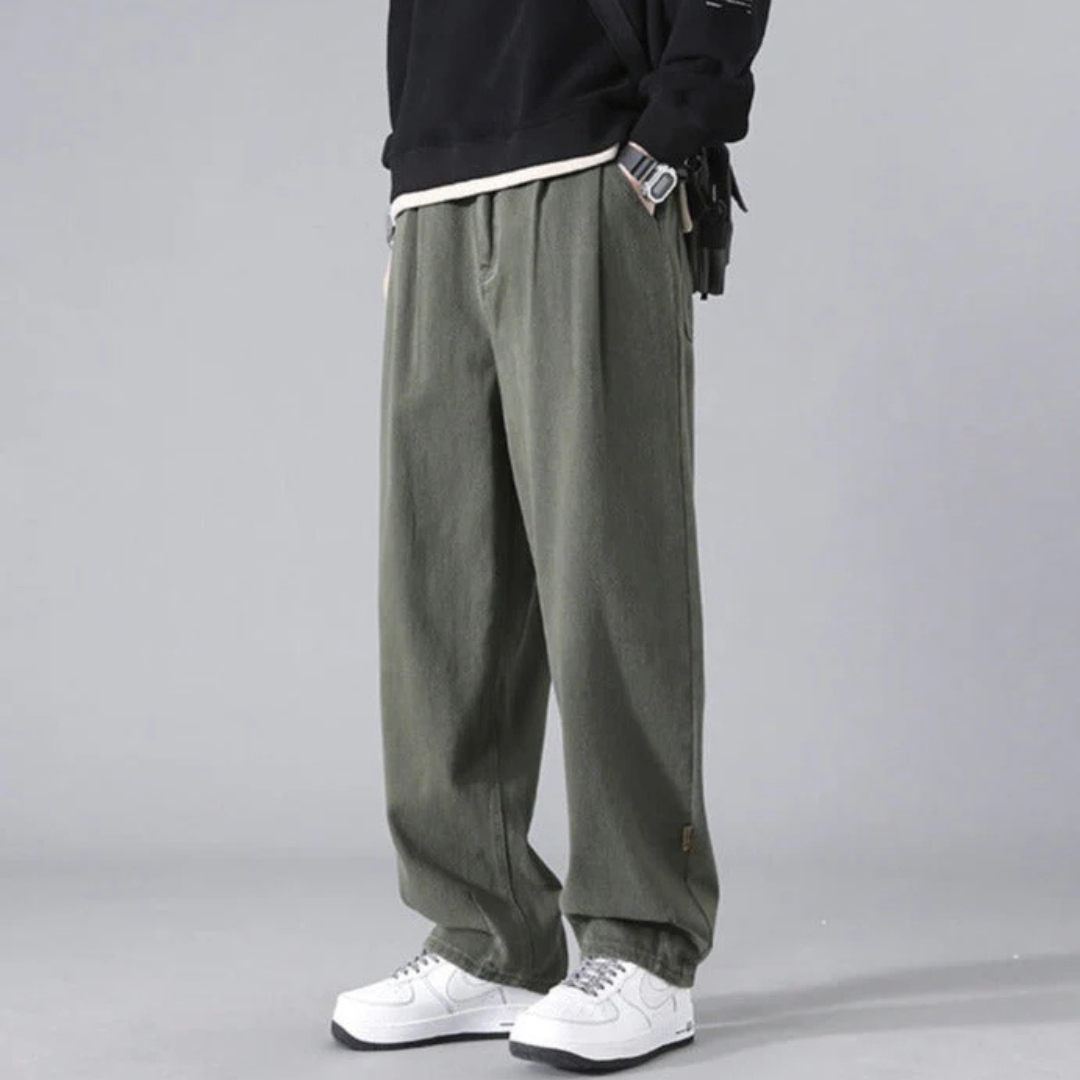 Graue, weite Herren-Cargohose aus Baumwolle, kombiniert mit weißen Sneakers und schwarzem Pullover. Modischer Streetwear-Look für Herren.