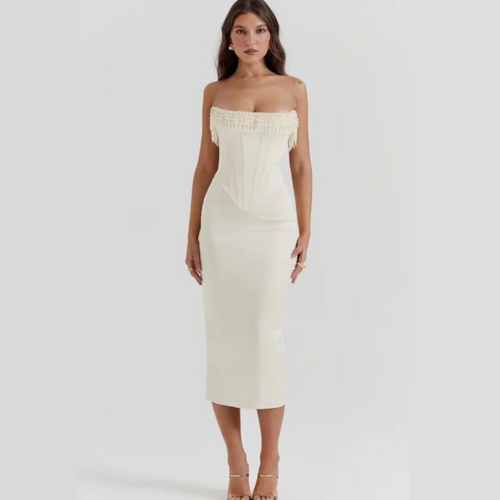 Frau in elegantem, cremefarbenem Korsettkleid mit Fransen, trägerlos, knielang, modisch, aufrecht stehend, vor neutralem Hintergrund.