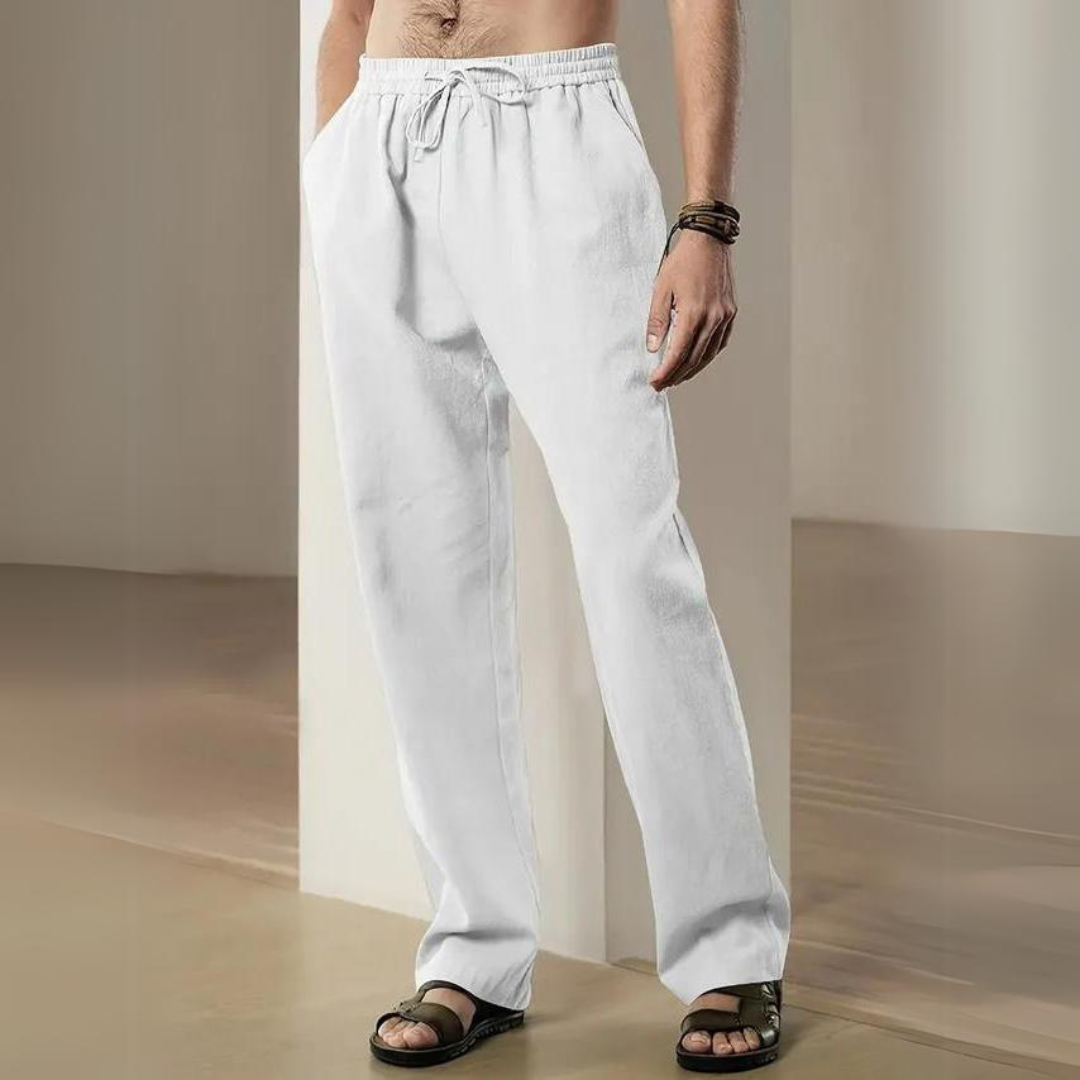 Mann trägt weiße Leinenhose, steht in modernem Raum. Bequeme Sommermode, lässiger Stil, ideal für Freizeit und Strand. Sandalen ergänzen Look.