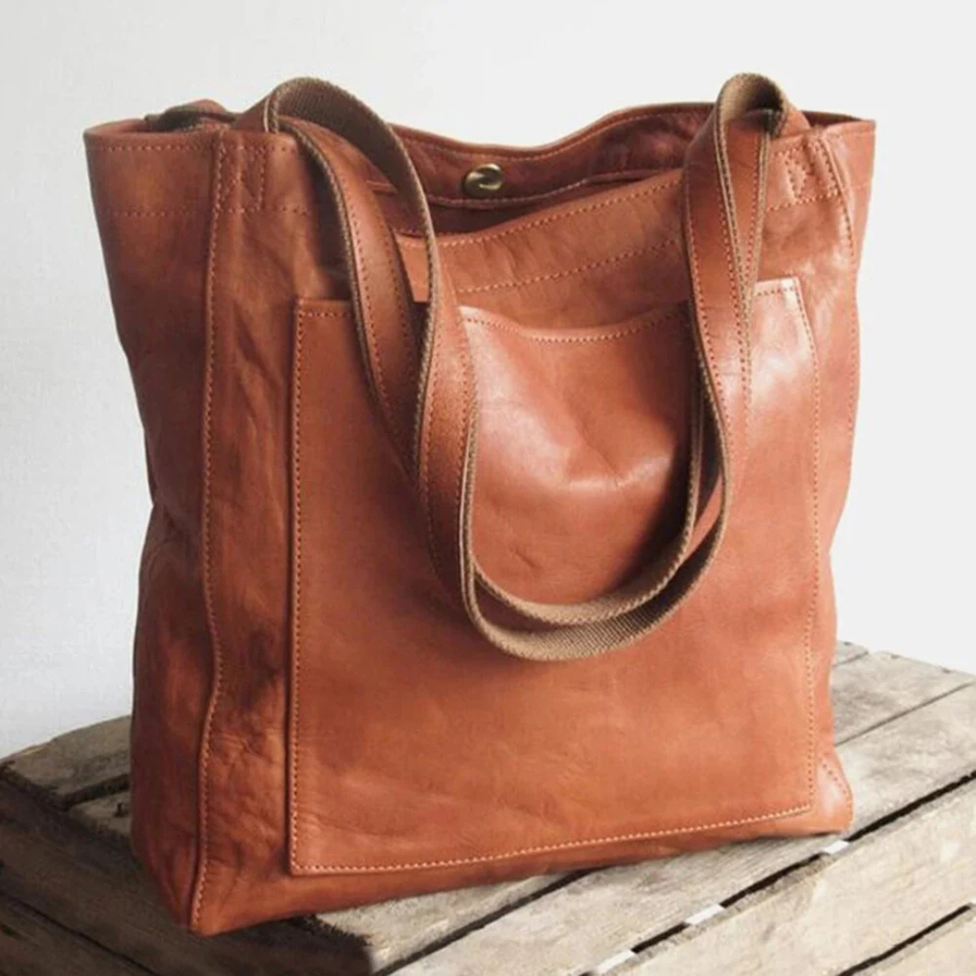 Braune Ledertasche mit doppelten Tragegriffen auf Holzkiste. Stilvolle, geräumige Handtasche für Damen. Perfekt für Alltag und Büro.