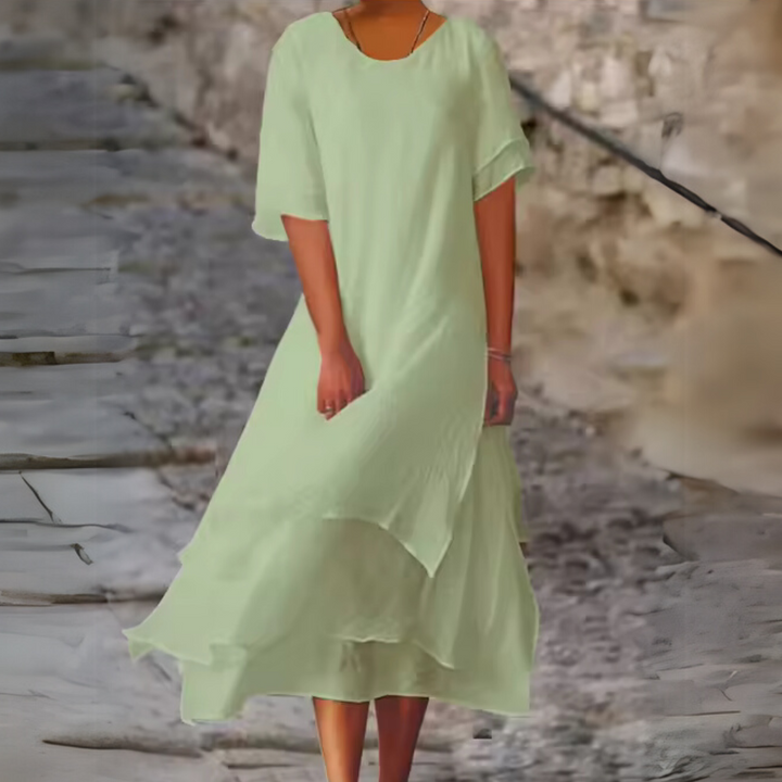 Frau in fließendem, mintgrünem Kleid auf gepflastertem Weg. Sommermode, elegantes Design, luftiger Stoff, Freizeitkleidung.
