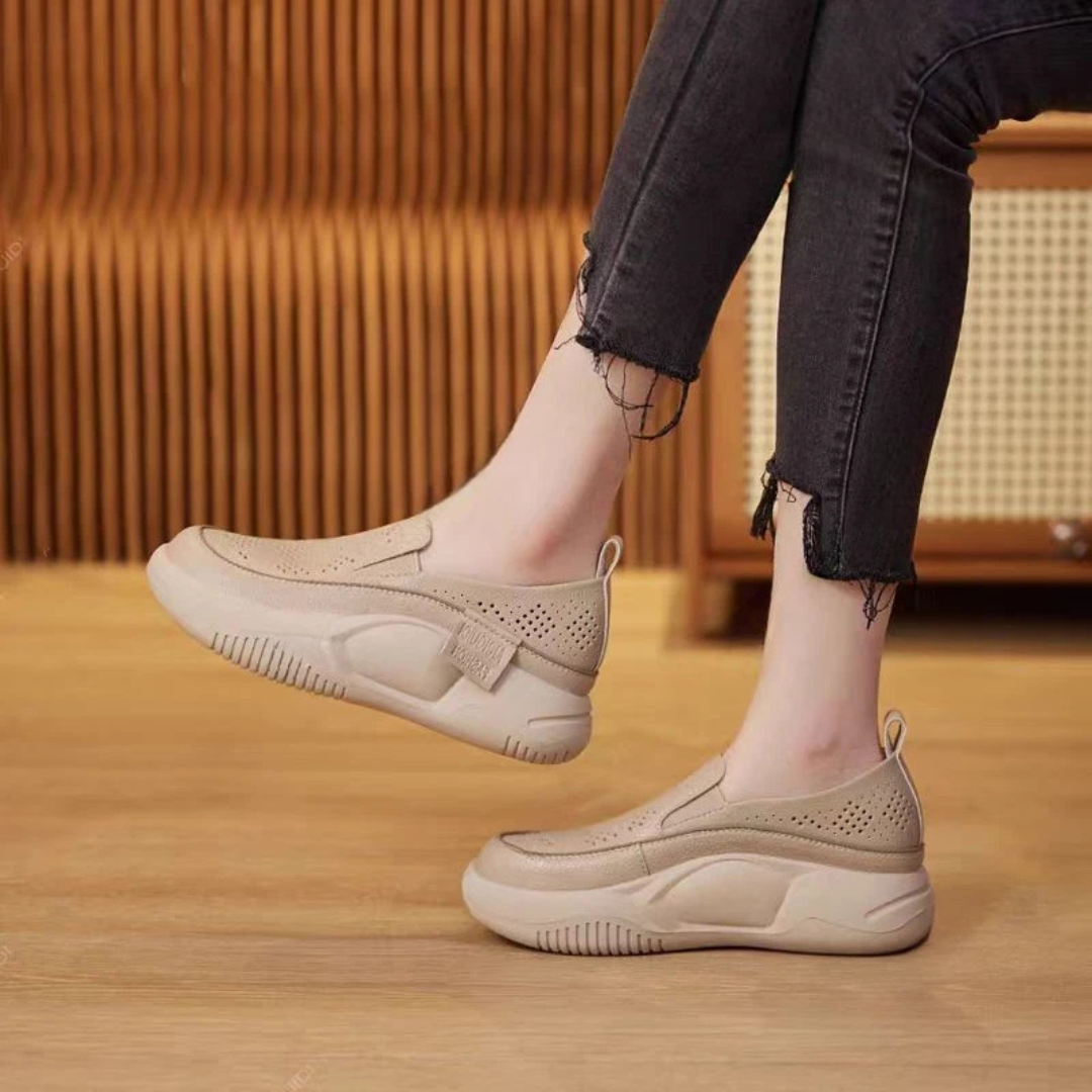 Beige Damen-Sneaker mit dicker Sohle, perforiertem Design und Klettverschluss, getragen mit schwarzen Jeans. Bequeme Freizeitschuhe für den Alltag.