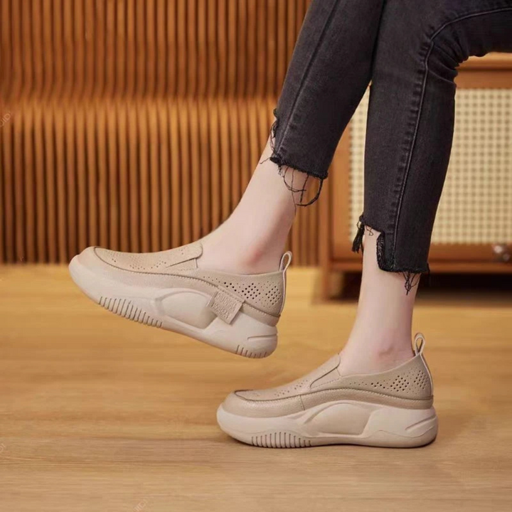 Beige Damen-Sneaker mit dicker Sohle, perforiertem Design und Klettverschluss, getragen mit schwarzen Jeans. Bequeme Freizeitschuhe für den Alltag.