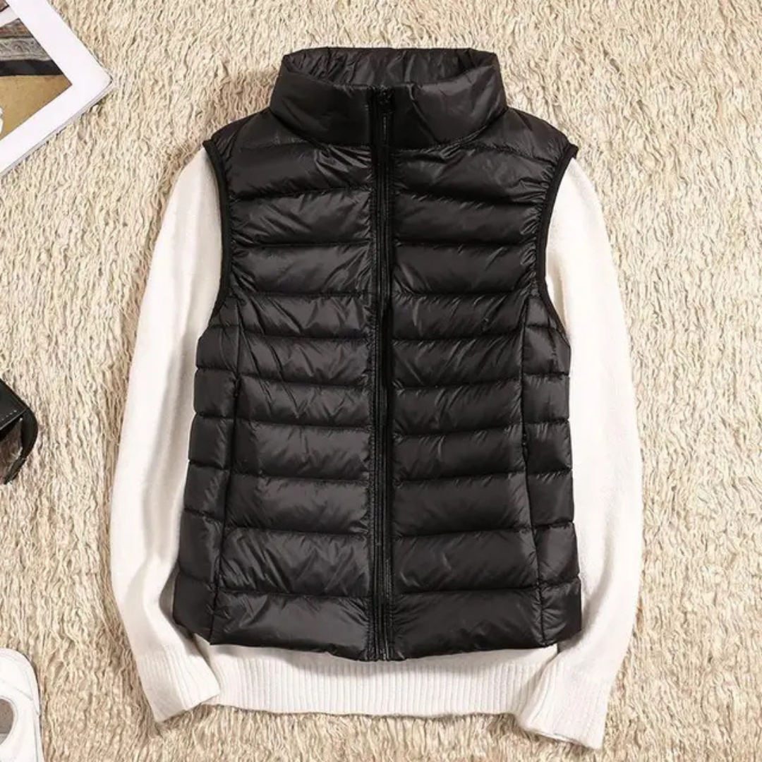 Schwarze Steppweste auf weißem Pullover, flach auf beigem Teppich. Modetrend, Winterbekleidung, warme Weste, stilvolle Damenmode.