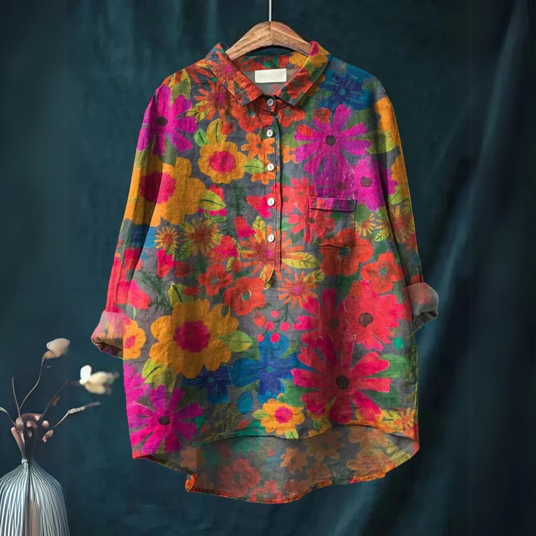 Bunte Damenbluse mit Blumenmuster, langärmlig, ausgestellt auf einem Kleiderbügel vor dunklem Hintergrund. Modetrend, farbenfrohe Kleidung.