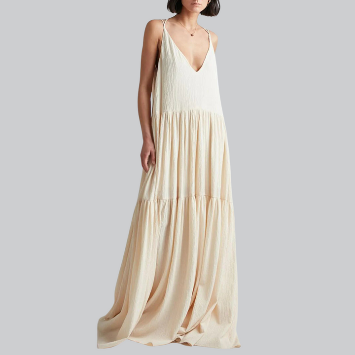 Frau in langem, ärmellosem, cremefarbenem Maxikleid mit V-Ausschnitt vor grauem Hintergrund. Elegantes Sommerkleid, Mode, Damenbekleidung.