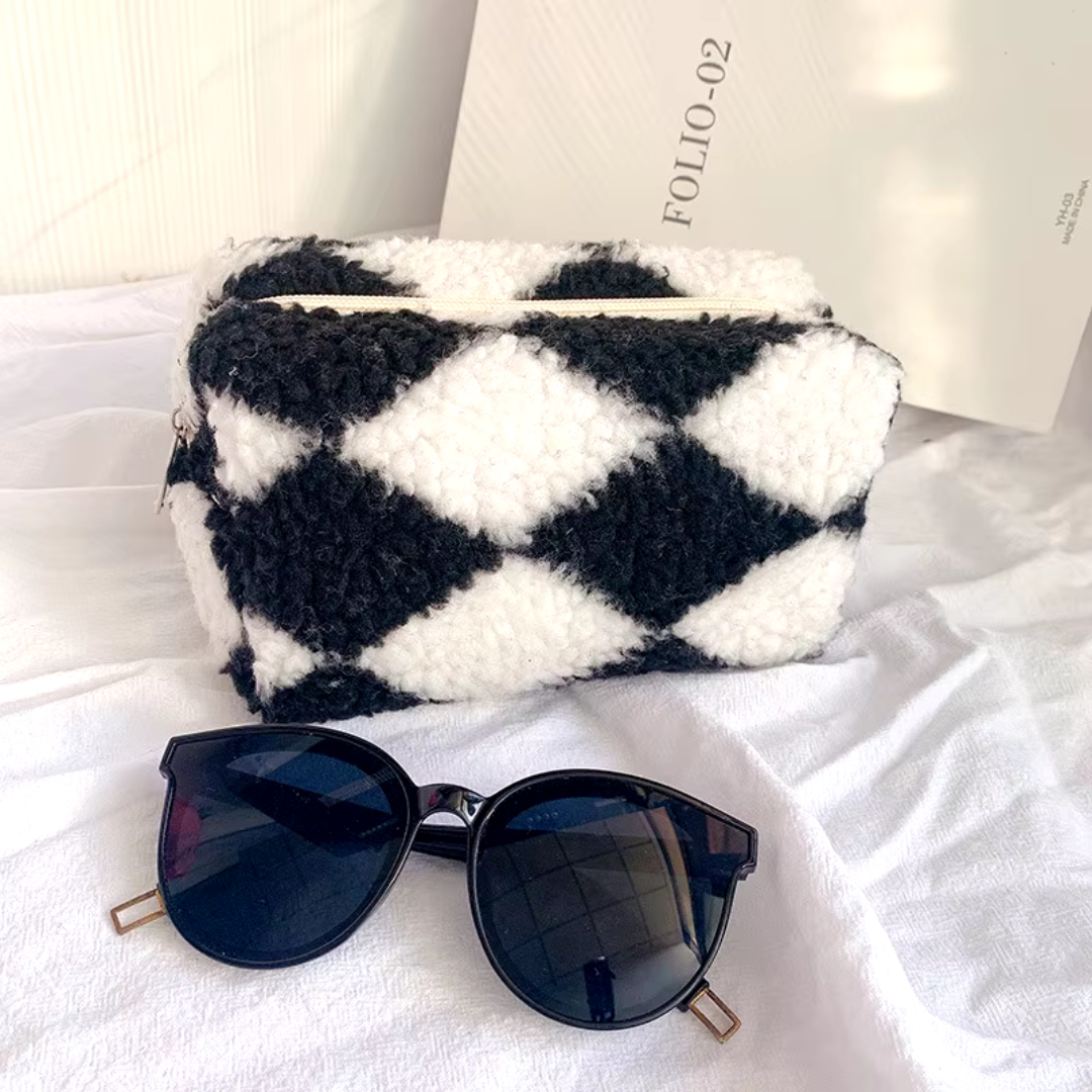Schwarz-weiße karierte Kosmetiktasche aus Plüsch neben stilvoller Sonnenbrille auf weißem Hintergrund. Modisches Accessoire-Set.
