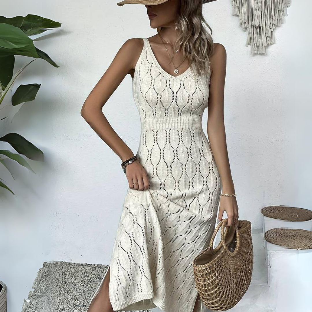 Frau in elegantem, cremefarbenem Strickkleid mit Strohhut und Korbtasche, steht vor weißer Wand mit Pflanzen. Sommermode, Boho-Stil, Damenbekleidung.