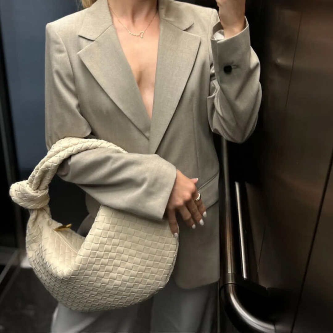 Frau im Aufzug mit beigem Blazer und geflochtener Tasche. Elegante Mode, Business-Look, stilvolle Damenbekleidung, Trend 2023.