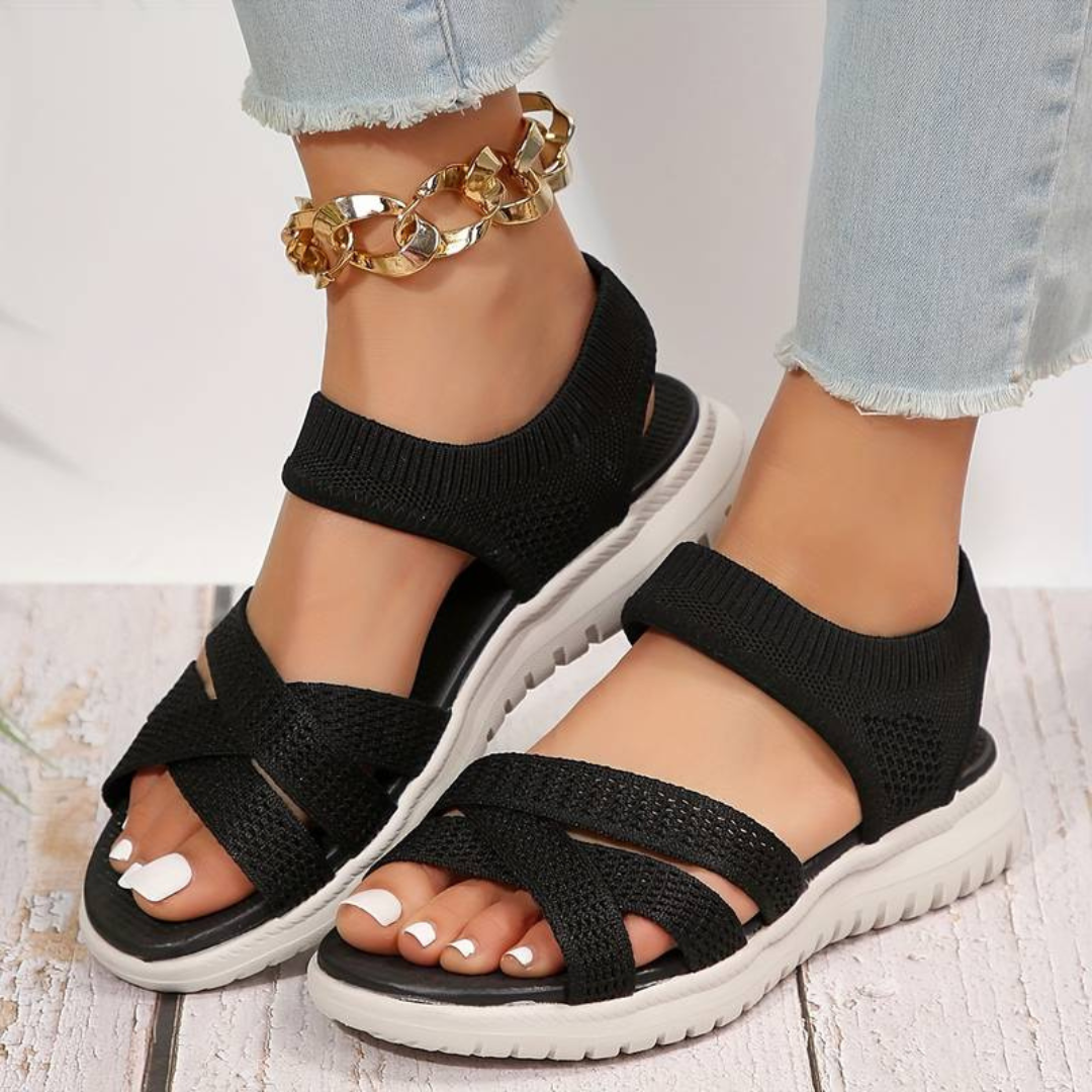 Schwarze Damen-Sandalen mit weißer Sohle, getragen mit hellblauen Jeans und goldener Fußkette. Bequeme Sommerschuhe, modisch und stilvoll.