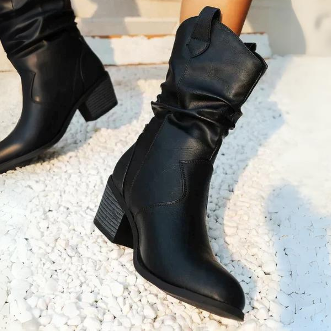 Schwarze Damenstiefel mit Blockabsatz auf weißem Kies. Modische, knöchelhohe Lederstiefel für Herbst und Winter. Elegante, robuste Schuhe.