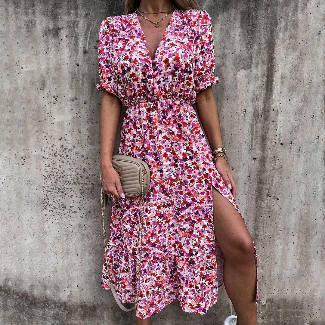 Frau in geblümtem Sommerkleid mit V-Ausschnitt und Beinschlitz, hält eine beige Umhängetasche, vor grauer Betonwand. Modetrend, Damenmode.