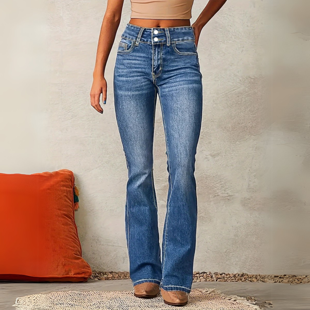 Frau in blauer Schlaghose, beige Top, vor grauer Wand. Modetrend, Damenjeans, High-Waist, Freizeitlook, stilvoll, modern, bequem.
