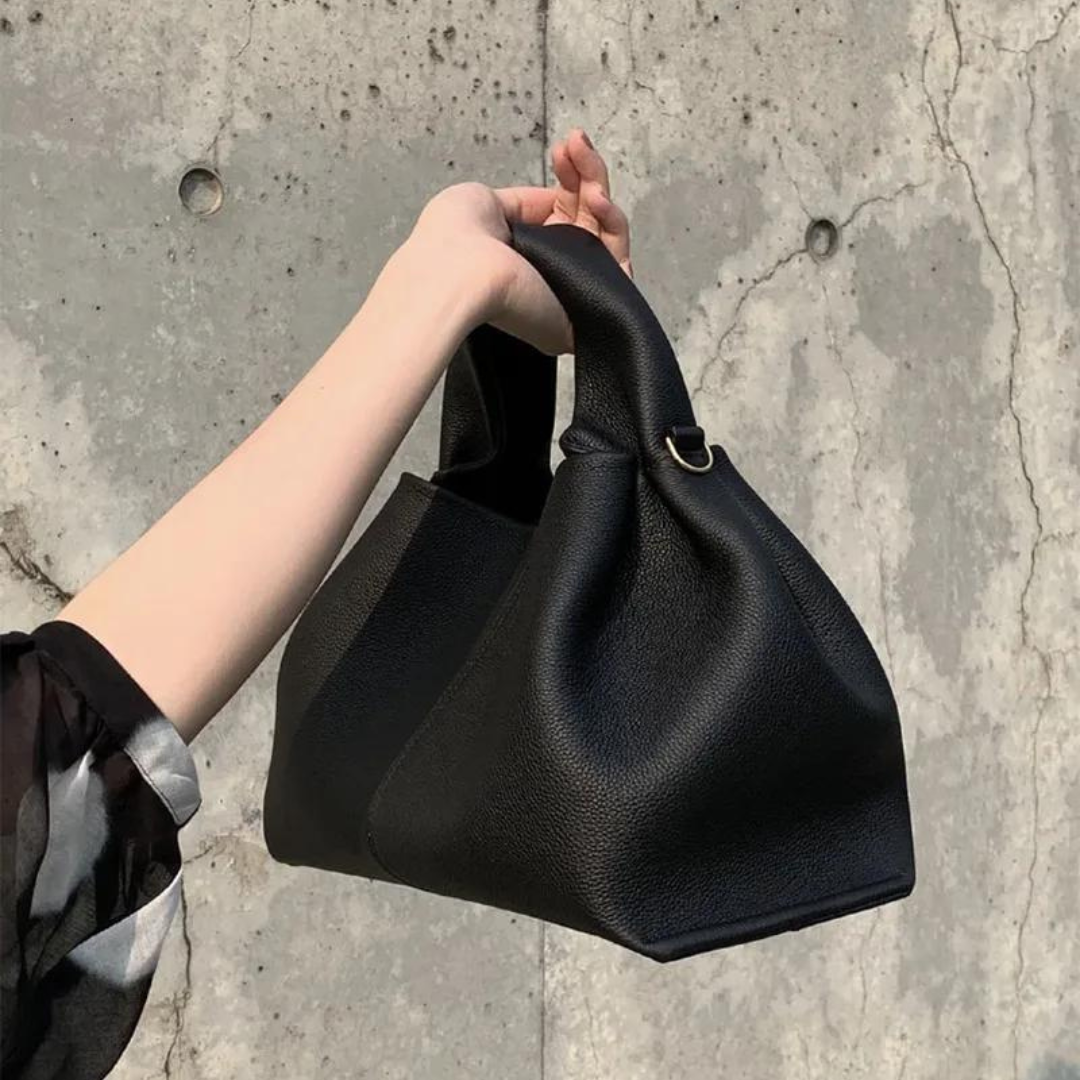 Schwarze Lederhandtasche in Hand gehalten vor Betonwand, modernes Design, minimalistisch, Damenmode, stilvolles Accessoire, Trend 2023.