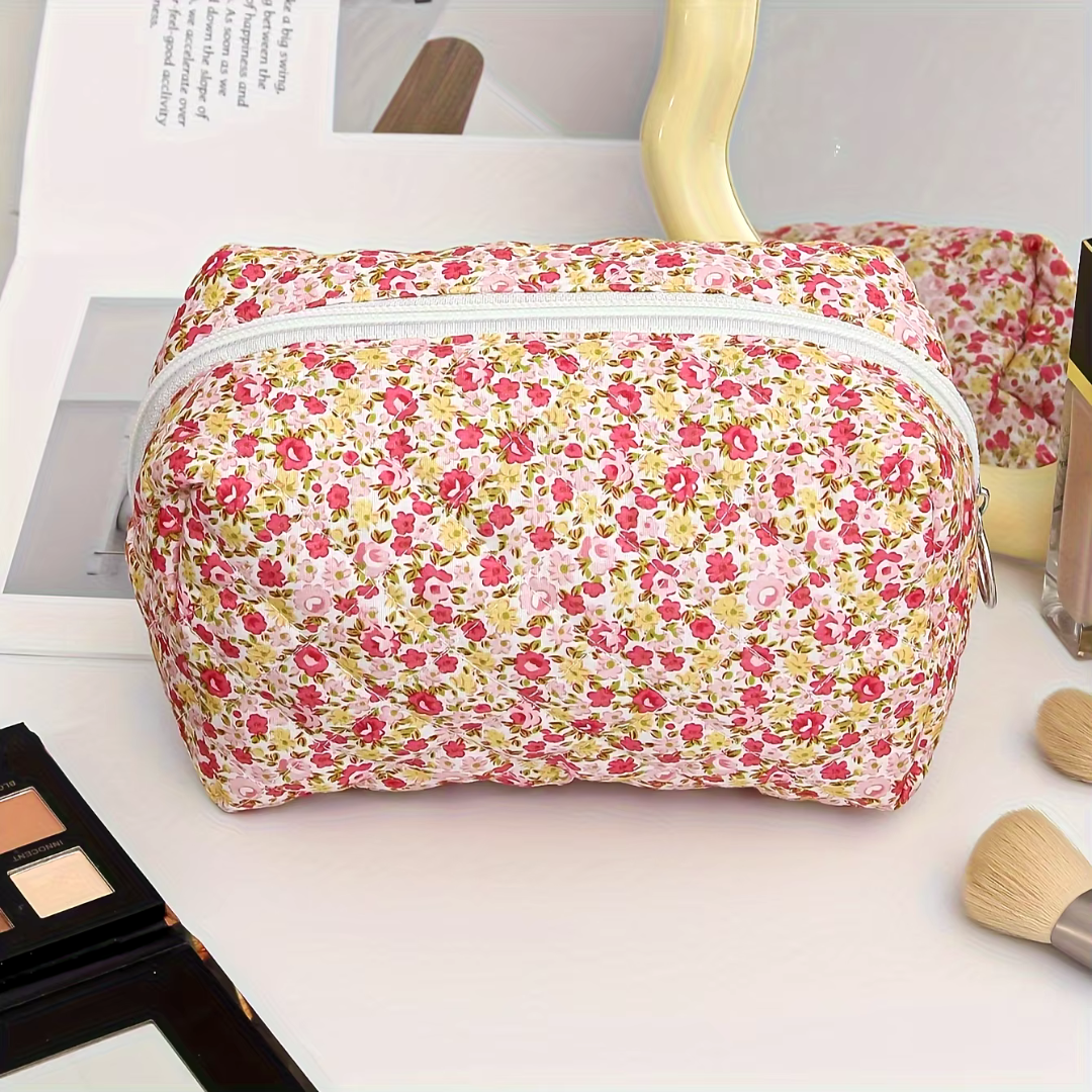 Blumige Kosmetiktasche mit Reißverschluss auf Schminktisch, umgeben von Make-up-Pinseln und Lidschattenpalette. Ideal für Reisen und Aufbewahrung.
