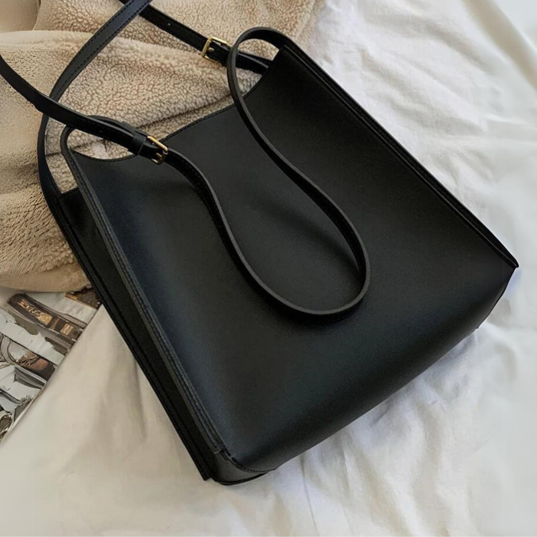Schwarze Ledertasche auf weißem Bett, elegantes Design, minimalistisch, hochwertige Handtasche, Modeaccessoire, Damenmode, stilvoll.