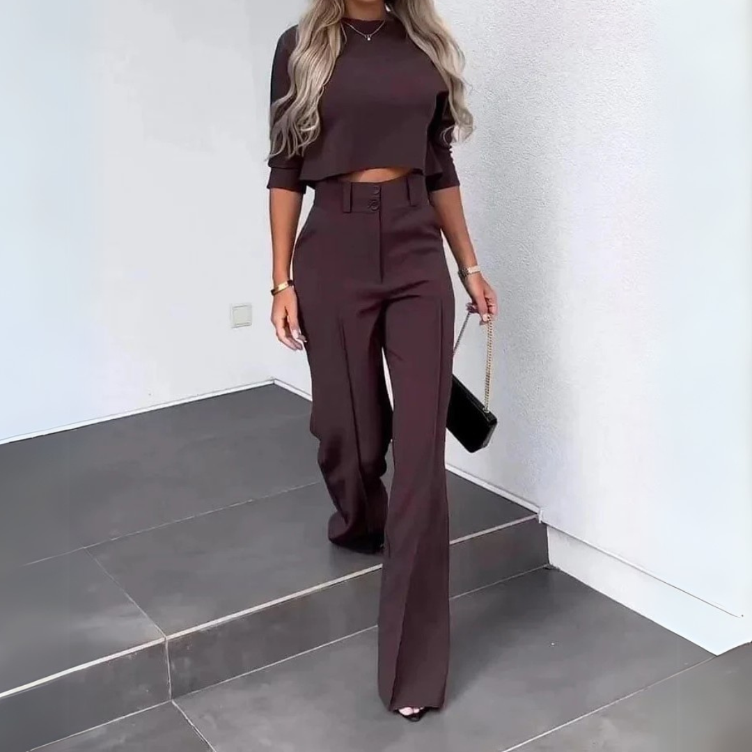 Frau in eleganter, dunkelbrauner Hose und passendem Crop-Top, trägt schwarze Handtasche, geht Treppe hinunter. Modetrend, stilvolle Damenbekleidung.