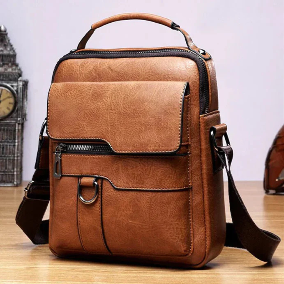Braune Ledertasche mit verstellbarem Schultergurt, mehreren Reißverschlusstaschen und robustem Griff auf Holztisch, ideal für Herrenmode und Business.