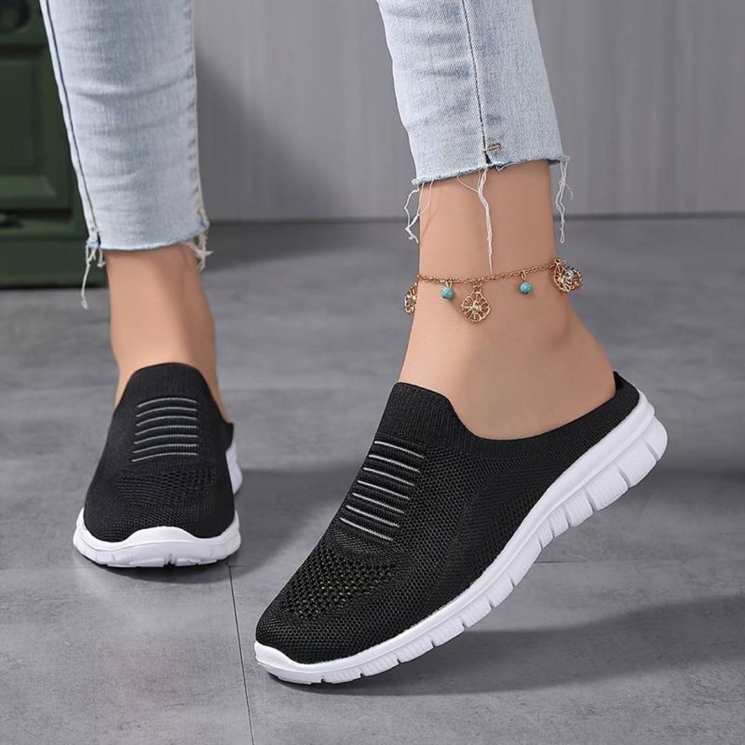 Schwarze Damen-Sneaker mit weißer Sohle, getragen mit hellblauen Jeans und einem goldenen Fußkettchen. Bequeme, modische Freizeitschuhe.