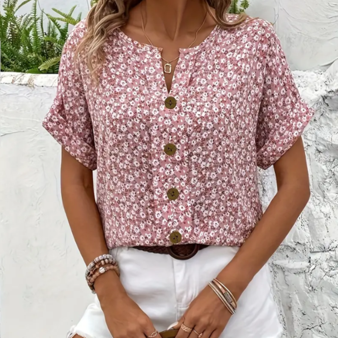 Frau trägt rosa geblümte Bluse mit Knopfleiste, kombiniert mit weißen Shorts. Sommermode, lässiger Stil, florales Muster, Damenbekleidung.