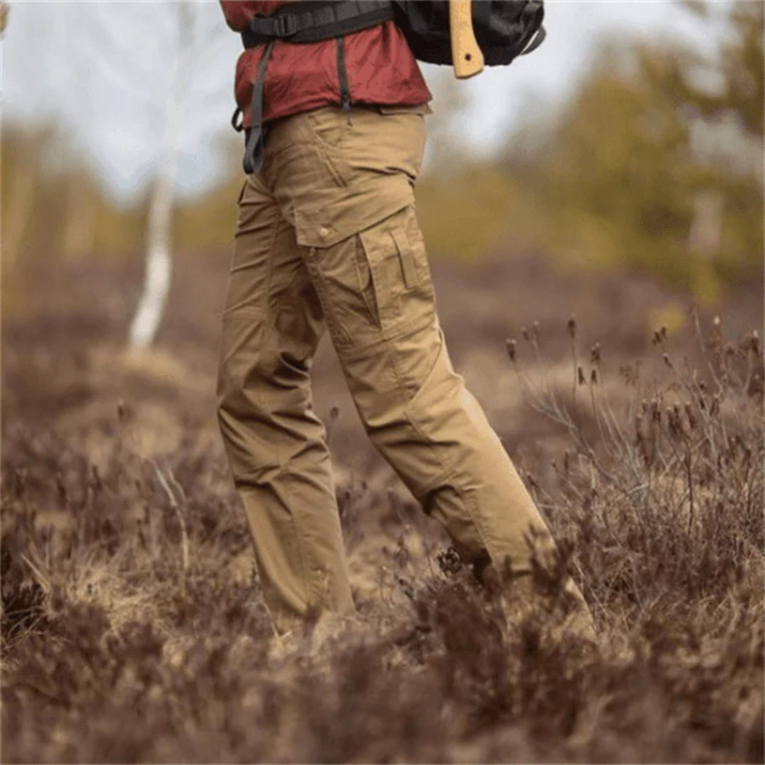 Person in Outdoor-Kleidung mit brauner Cargohose und roter Jacke wandert durch herbstliche Landschaft. Wandern, Outdoor-Abenteuer, Naturerlebnis.