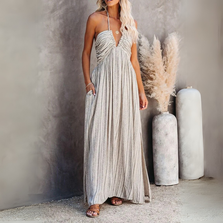 Elegantes, langes Sommerkleid in Beige mit Spaghettiträgern, getragen von einer Frau. Neben ihr stehen dekorative Pampasgräser in einer Vase.