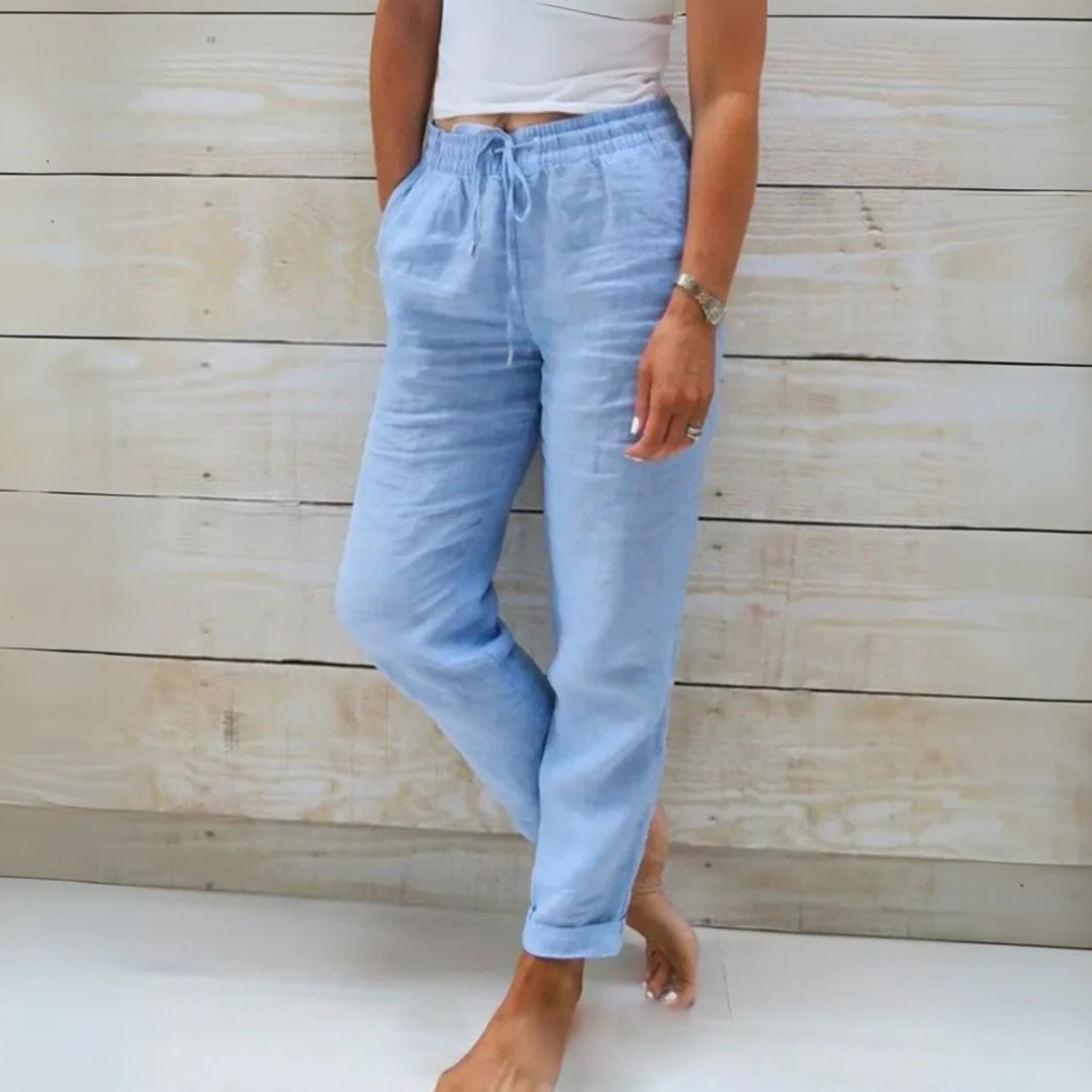 Damen in hellblauer Leinenhose und weißem Top vor Holzwand. Sommermode, lässiger Stil, bequeme Kleidung, Freizeitlook.