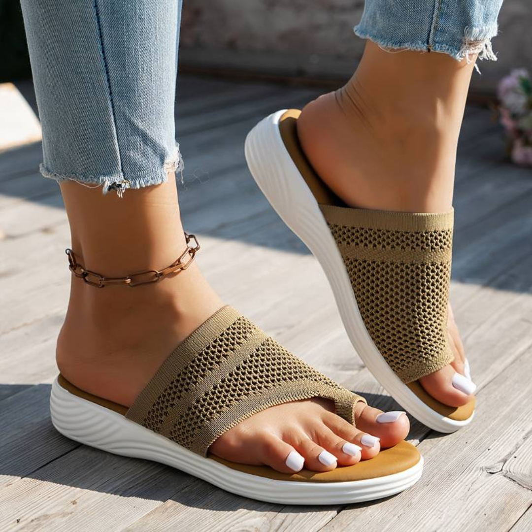 Damenfüße in beigen, atmungsaktiven Sandalen mit Keilabsatz und Zehenschlaufe, kombiniert mit hellblauen Jeans. Perfekt für Sommermode und Komfort.
