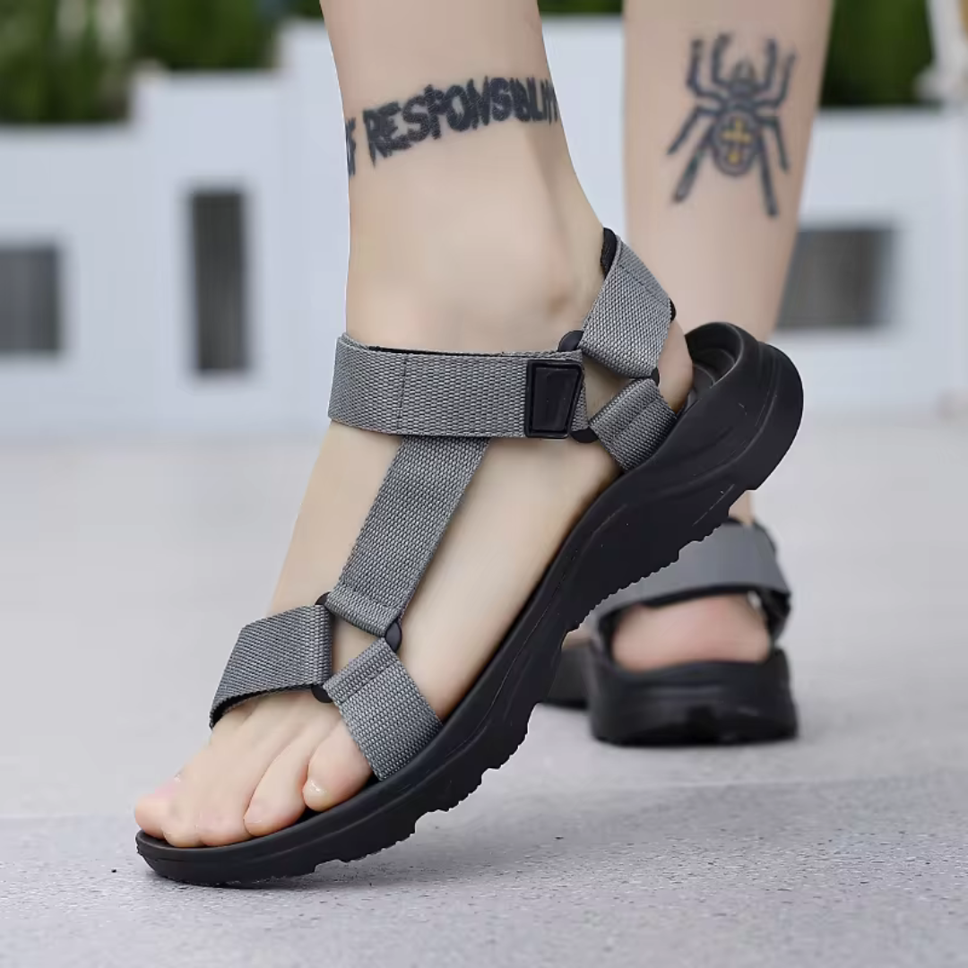 Graue Outdoor-Sandalen mit verstellbaren Riemen an Füßen mit Tattoos. Bequeme, rutschfeste Wandersandalen für Damen und Herren.