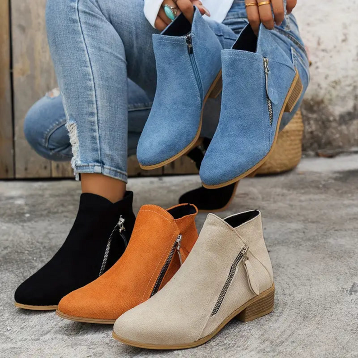 Damenstiefeletten in Blau, Schwarz, Orange und Beige mit Reißverschluss, präsentiert auf Betonboden. Modische Herbstschuhe, ideal für Jeans.