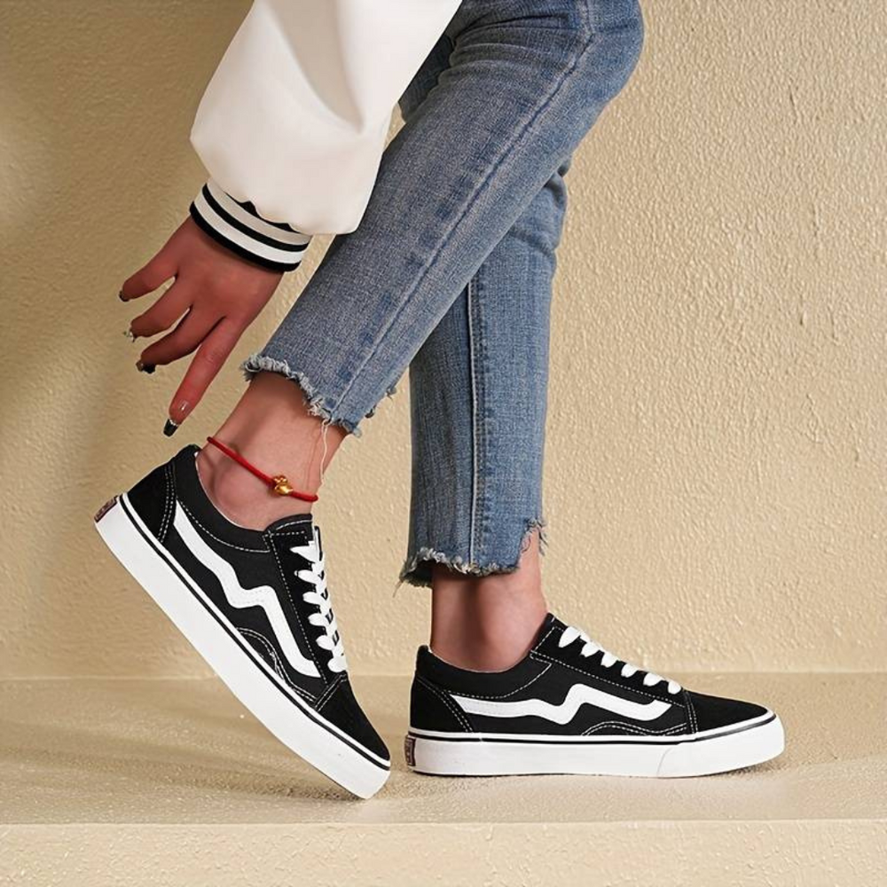Schwarze Sneaker mit weißem Streifen, getragen von Person in blauen Jeans. Modische Freizeitschuhe, ideal für urbanen Streetstyle.