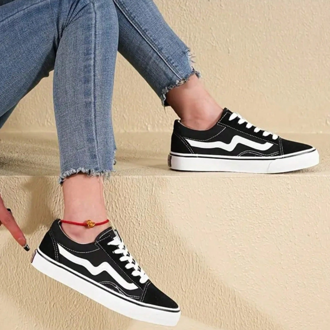 Schwarze Sneaker mit weißem Streifen, getragen von Person in blauen Jeans. Modische Freizeitschuhe, ideal für urbanen Streetstyle.