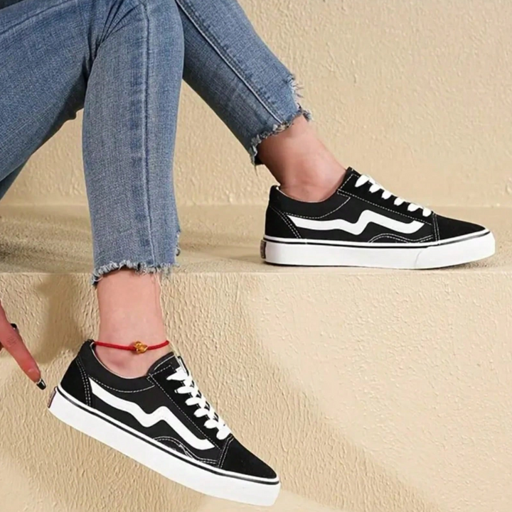 Schwarze Sneaker mit weißem Streifen, getragen von Person in blauen Jeans. Modische Freizeitschuhe, ideal für urbanen Streetstyle.