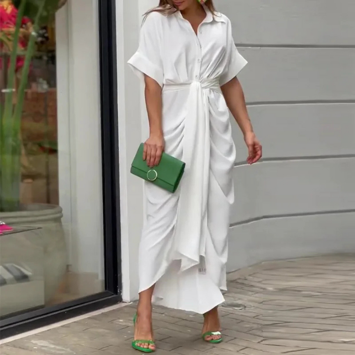 Frau in elegantem weißen Maxikleid mit Drapierung, hält grüne Clutch. Sommermode, stilvolle Abendgarderobe, trendige Accessoires.