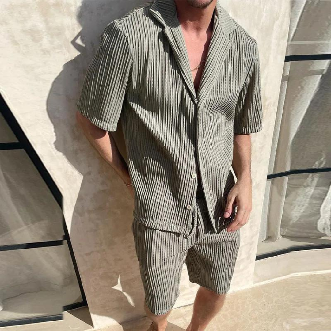 Mann in gestreiftem, kurzärmligem Hemd und Shorts aus Leinen, steht vor beigem Hintergrund. Sommermode, Herrenbekleidung, Freizeitlook.