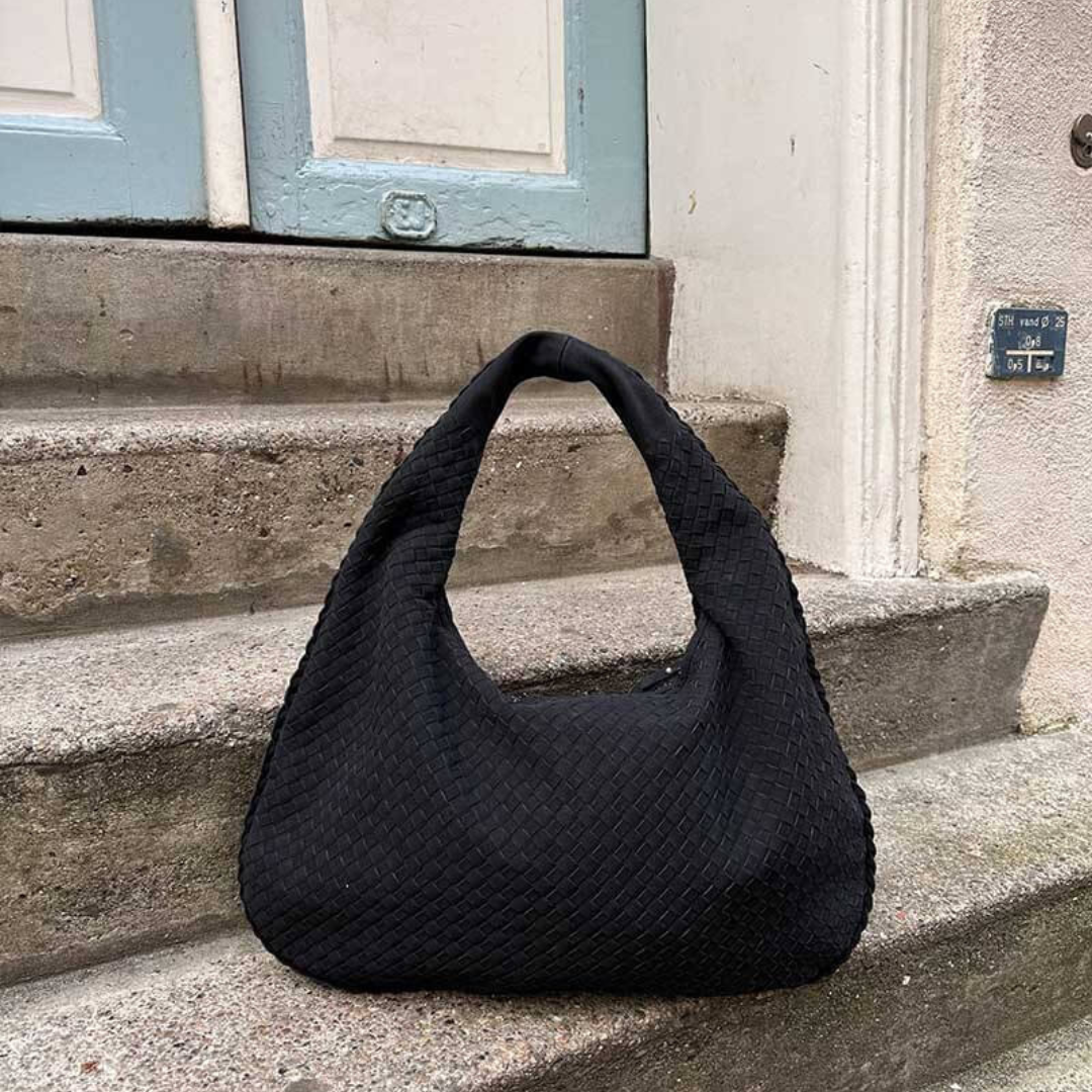 Schwarze geflochtene Handtasche auf Steintreppe vor blauer Tür, modisches Accessoire, elegantes Design, Damenmode, stilvolle Tasche.