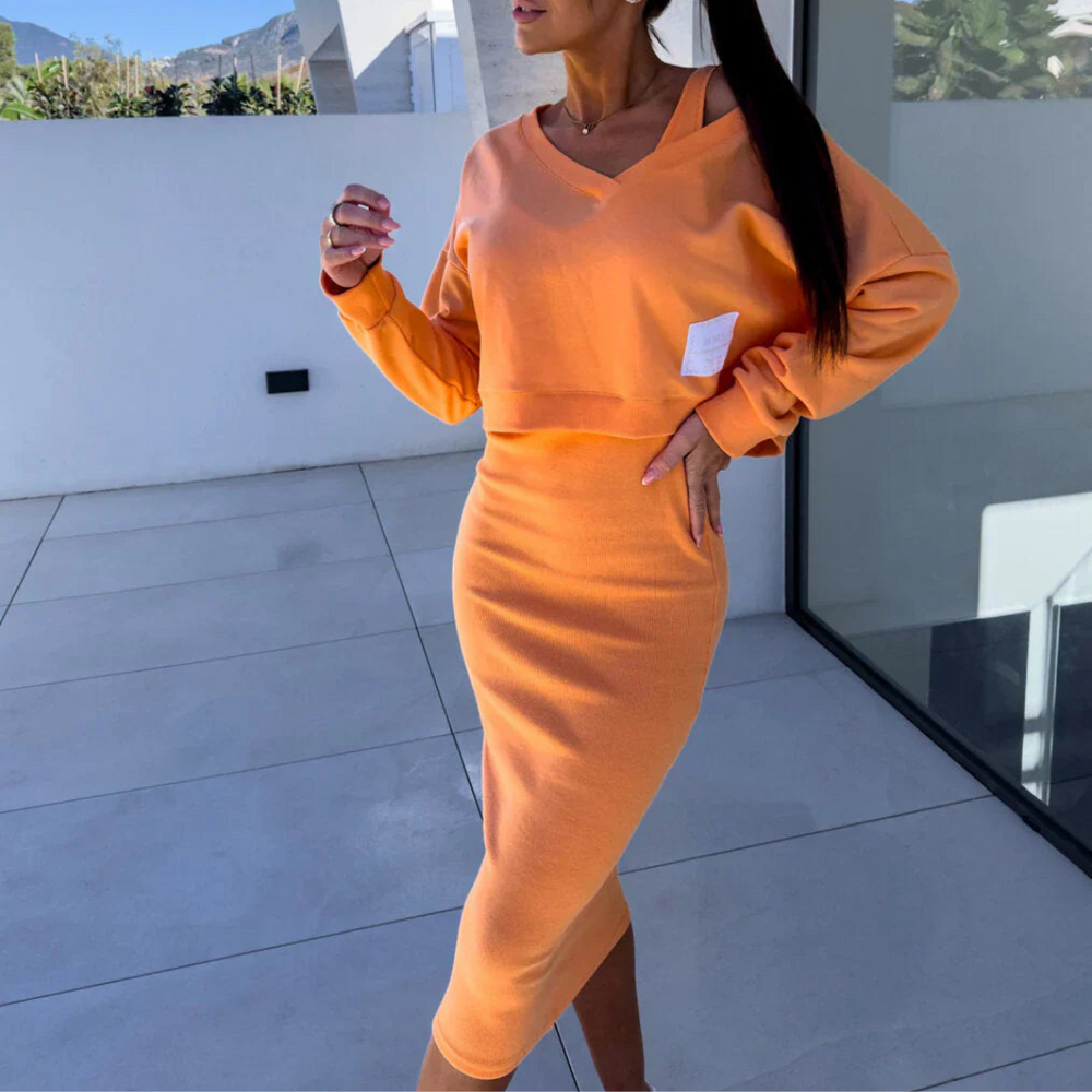 Frau in orangefarbenem, langärmligem Kleid mit V-Ausschnitt, steht auf Terrasse. Modernes Design, modische Damenbekleidung, stilvoller Look.