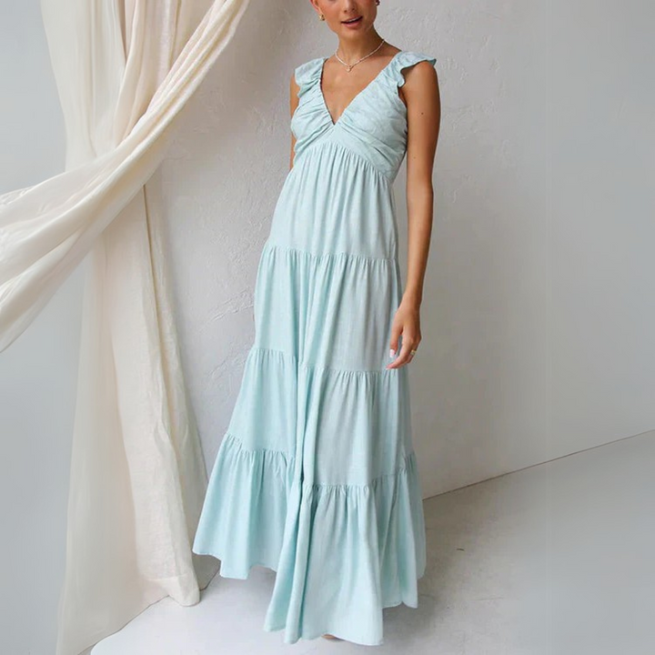 Frau in langem, hellblauem Sommerkleid mit Rüschenärmeln steht vor weißem Hintergrund. Elegantes, luftiges Maxikleid für Damenmode.