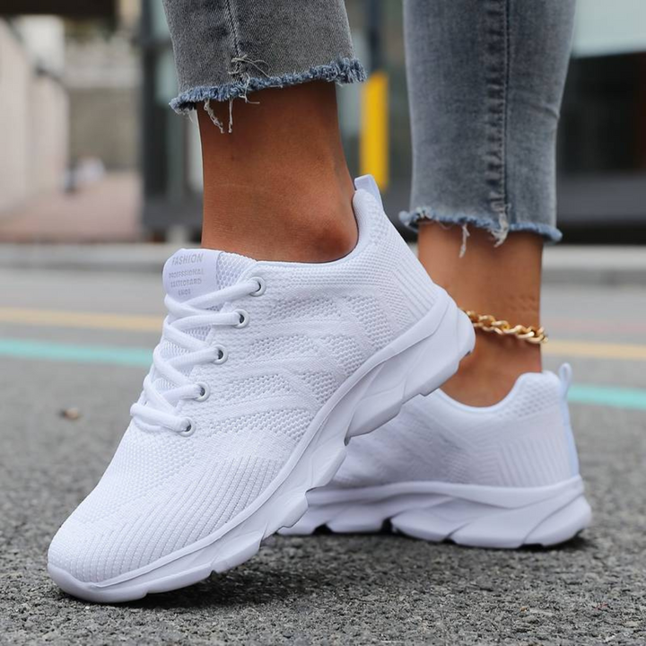 Weiße Damen-Sneaker auf Asphalt, getragen mit zerrissenen Jeans. Modische Sportschuhe, ideal für Freizeit und Streetwear.