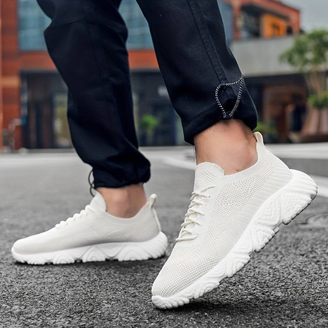 Weiße Sneaker auf Asphalt, getragen von Person in schwarzer Hose. Moderne, atmungsaktive Sportschuhe, ideal für urbanen Stil und Komfort.