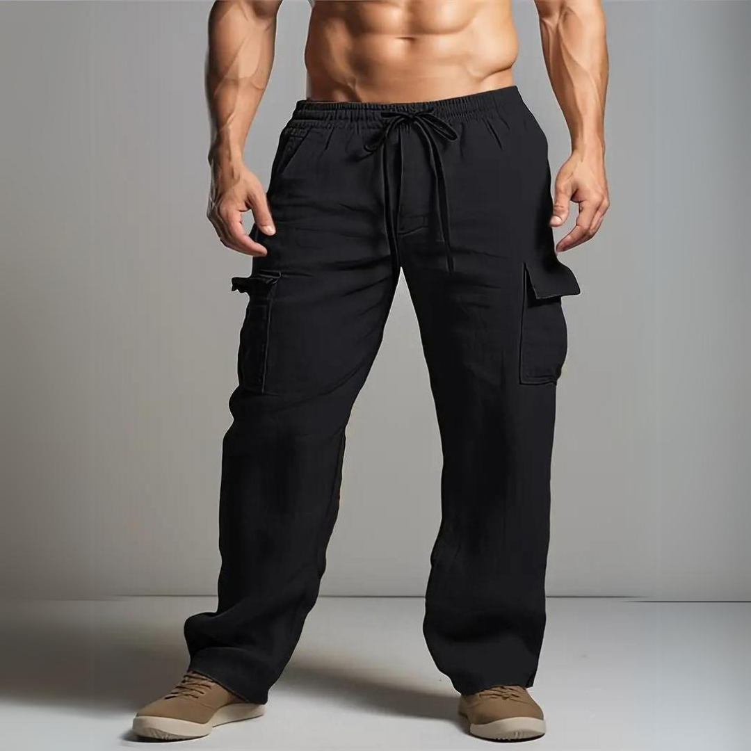 Mann in schwarzen Cargo-Hosen, muskulöser Oberkörper, beige Schuhe, grauer Hintergrund. Herrenmode, Freizeitkleidung, Fitness, stilvoll.